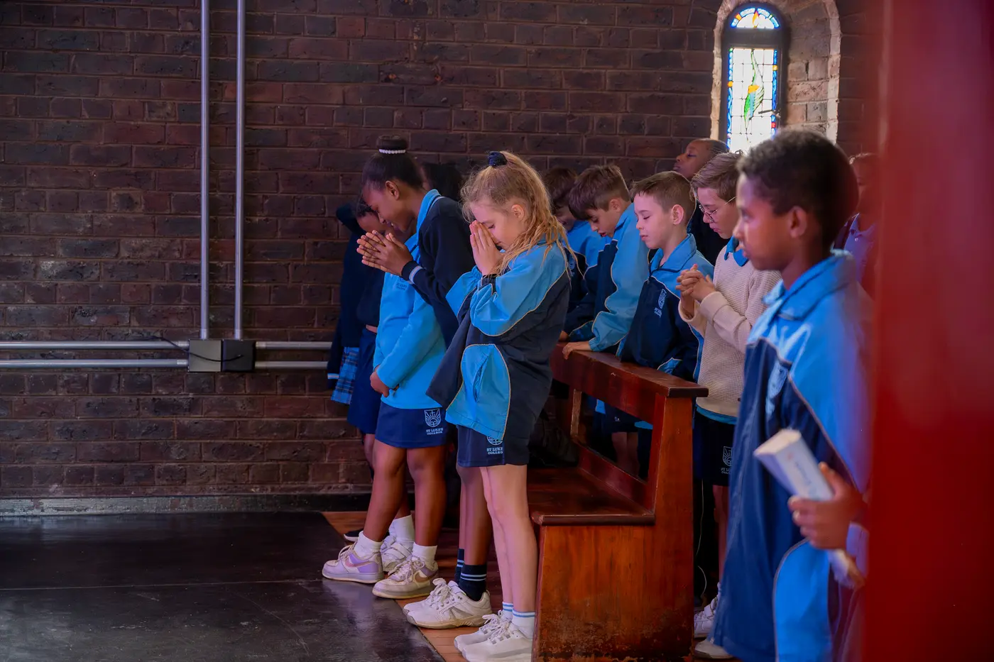 Children bowing their heads in prayer in the chapel pews