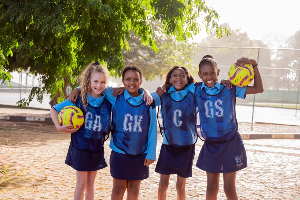 Four Preparatory School netball players smiling with their arms around each other