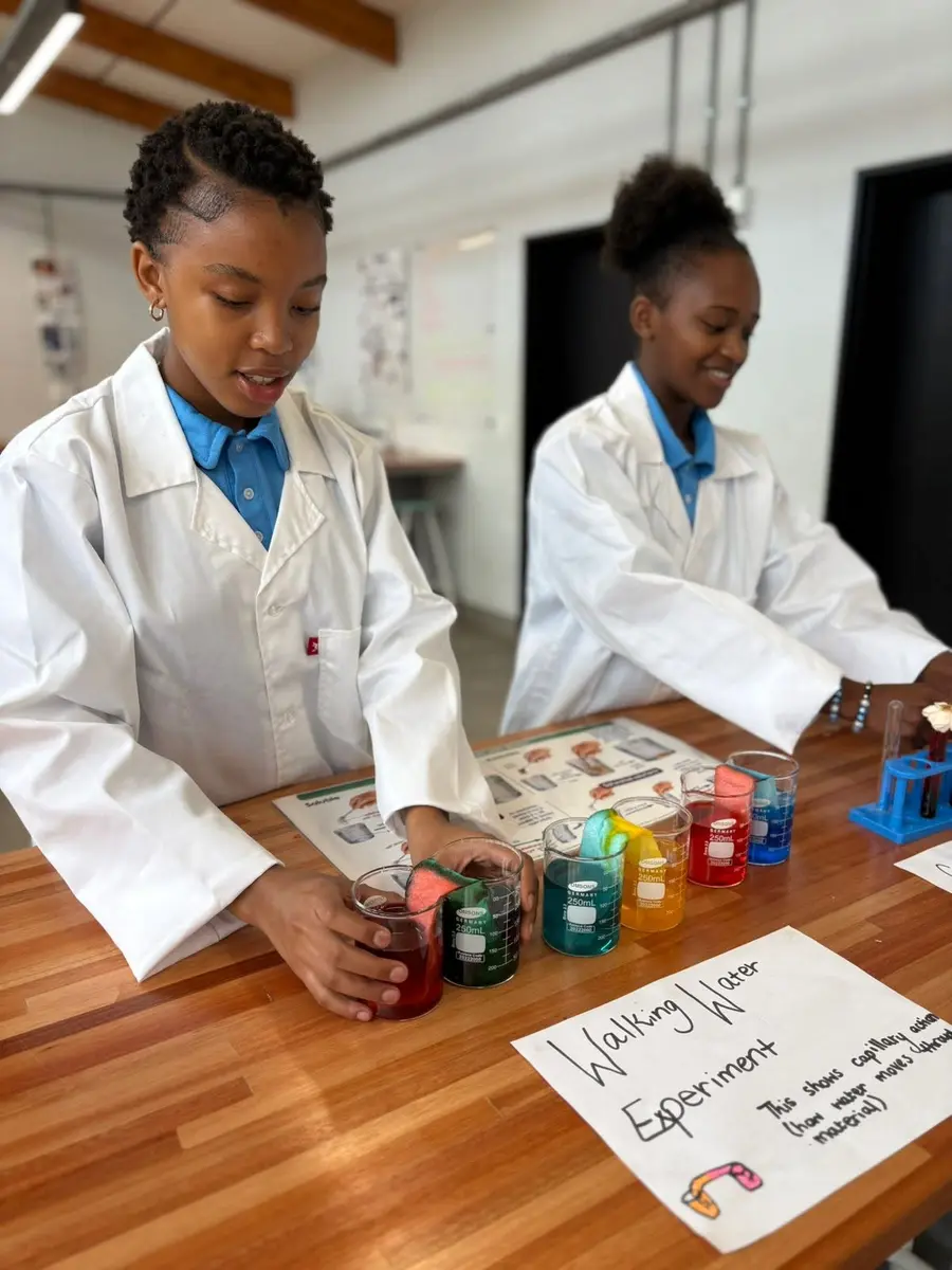 Two students in lab coats running a science experiment with coloured water