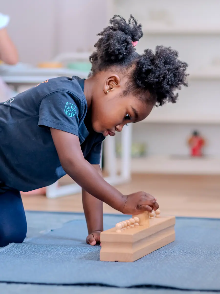 A preschool girl kneeling to work with wooden cylinder blocks