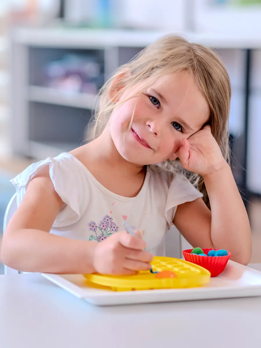 A preschool girl smiling with her chin in her hand at the table