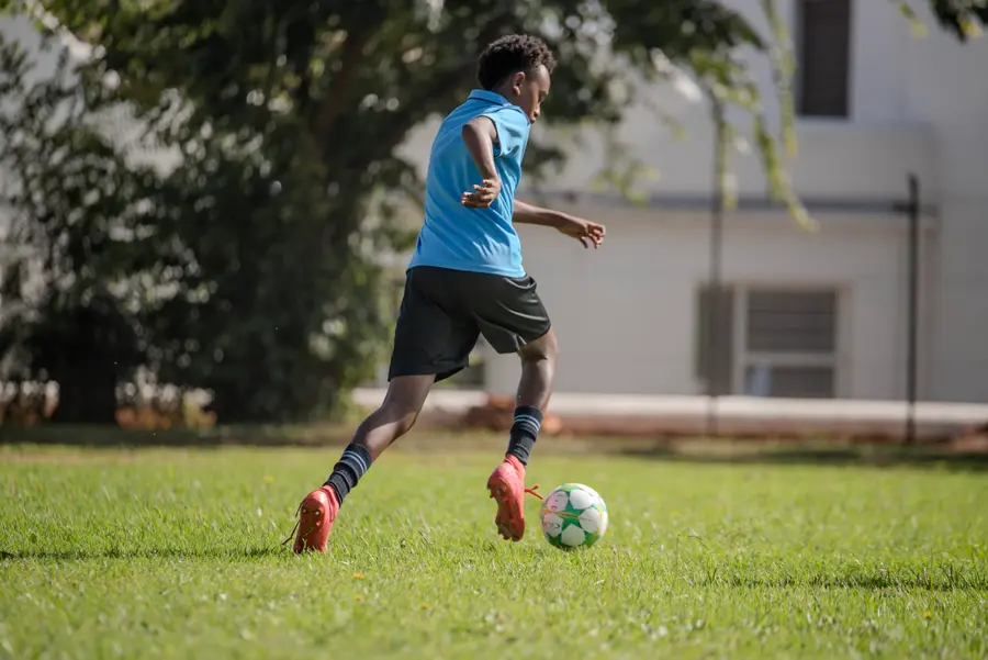 A student dribbling a soccer ball across the playing fields