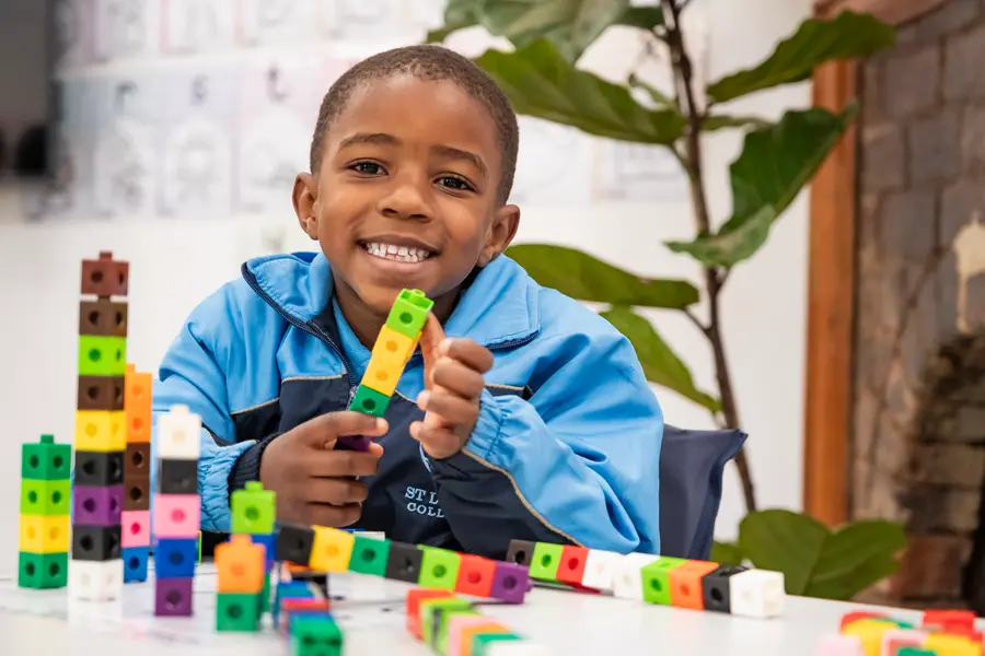 A smiling Preparatory School boy holding up a tower of counting blocks