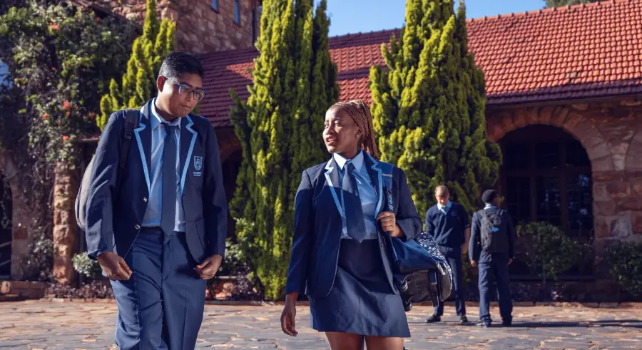 Students in blazers walking across the quad in front of the stone buildings