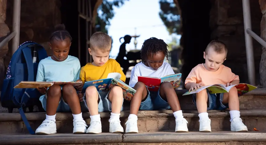 Four young children reading books together on stone steps