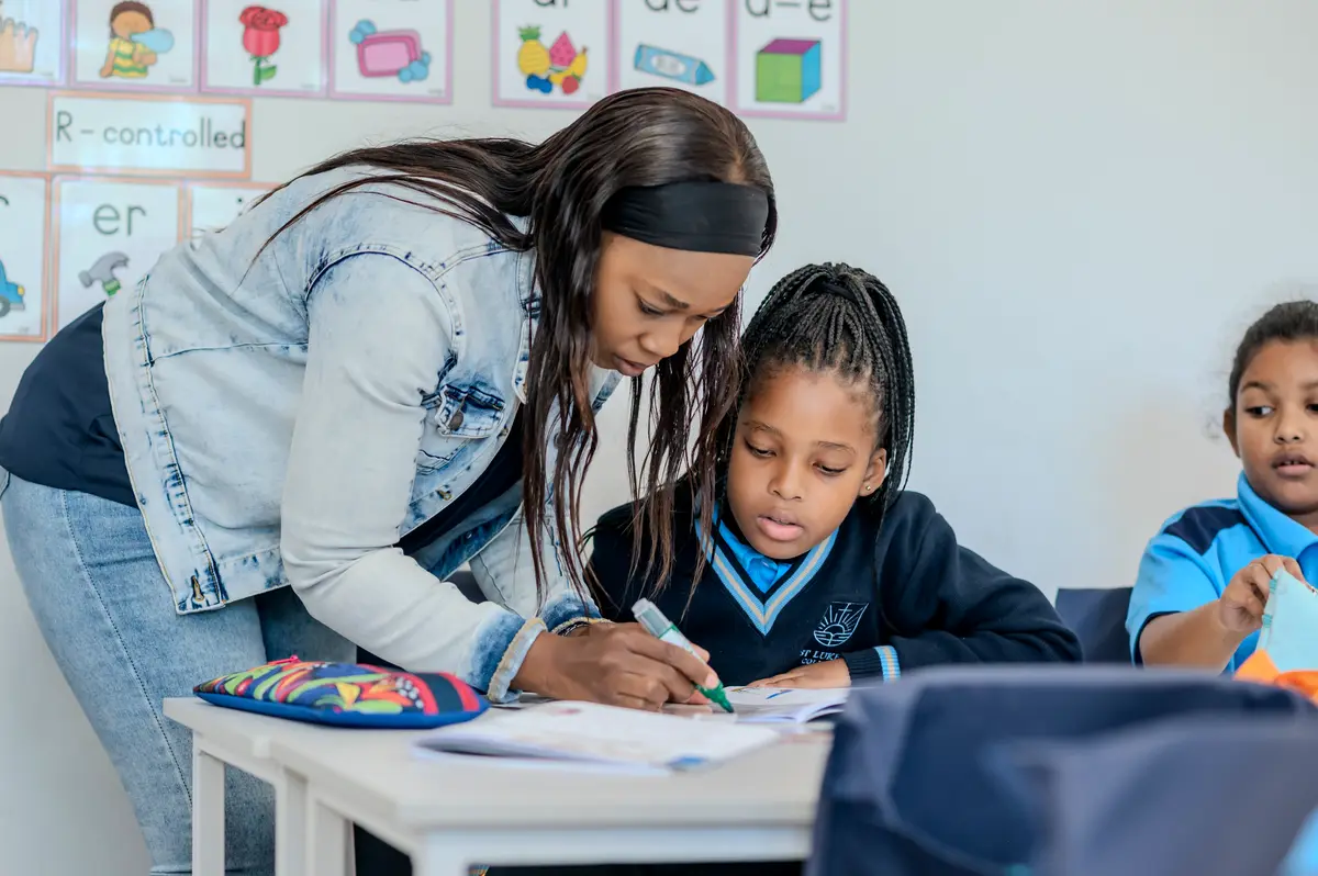 A teacher leaning in to help a Preparatory School girl with her work