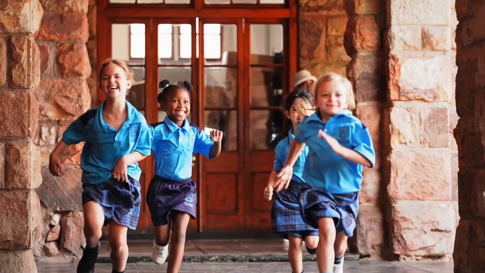 Children running and laughing along the stone colonnade at St Luke's College